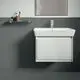 Waschtisch von Ideal Standard mit integriertem Waschbecken und einem Schubladenelement darunter, an einer modernen Wand installiert. Holzregal daneben für Utensilien.